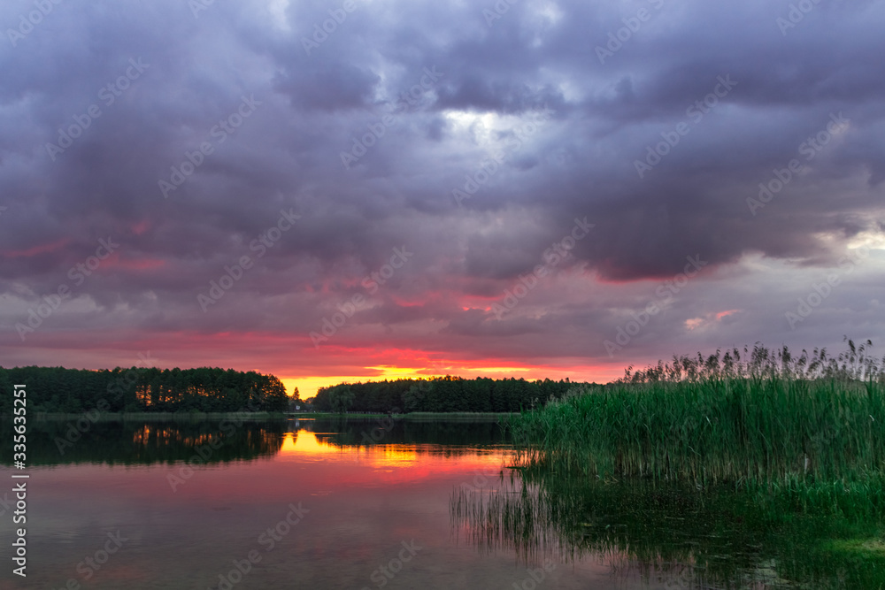 bright sunset over a forest lake with voluminous clouds