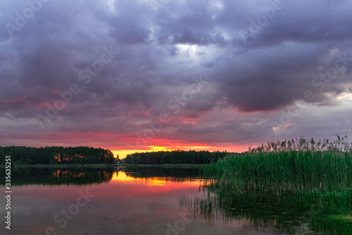 bright sunset over a forest lake with voluminous clouds © Павло Добиш