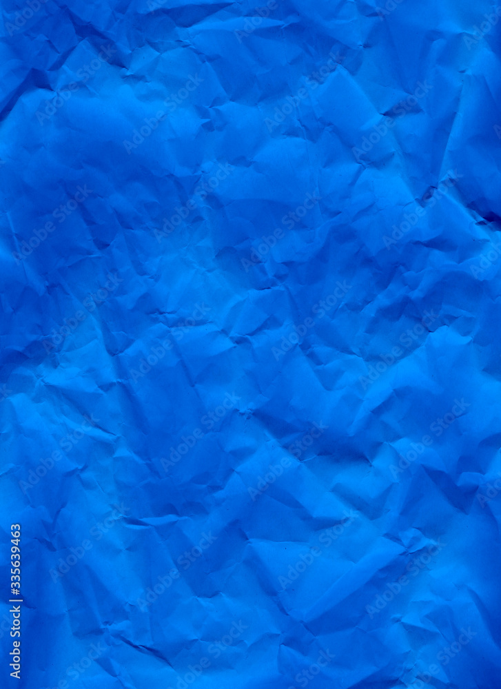 Blue crumpled paper texture background. A close-up abstract macro photo of creased paper. Abstract flatlay, top view. Vertical format. Free space for your text. Ultramarine colored