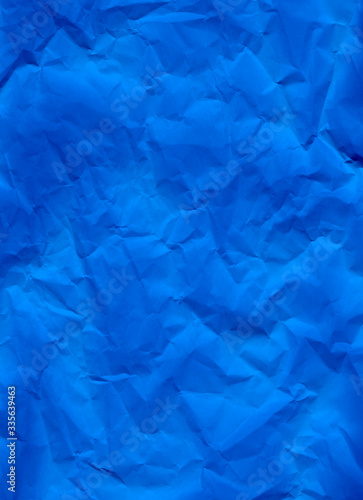 Blue crumpled paper texture background. A close-up abstract macro photo of creased paper. Abstract flatlay, top view. Vertical format. Free space for your text. Ultramarine colored