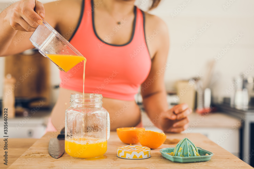 Young woman in sportswear pouring freshly squeezed orange juice in a jar. Young woman in sportswear pouring freshly squeezed orange juice in a jar.