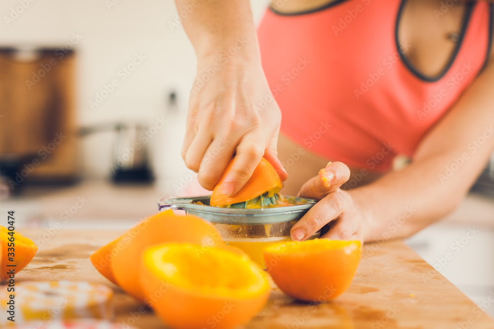 Young woman in sportswear squeezing oranges on a table, preparing juice.