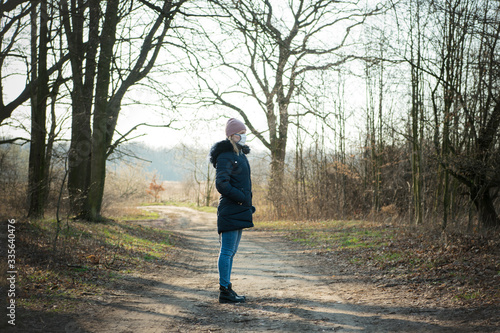 Sick woman with a hat alone on a walk in the forest, wearing protective mask against transmissible infectious diseases and as protection against the flu or coronavirus in public place. Coronavirus