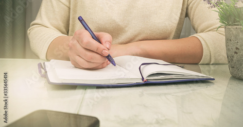 woman writes in paper notebook with purple pen near pot plant closeup