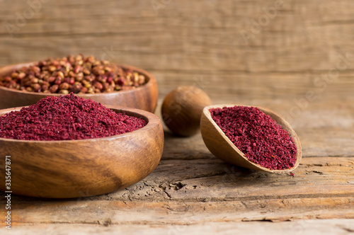 Dried ground red Sumac powder spices in wooden spoon with sumac berries on rustic table. Healthy food concept photo