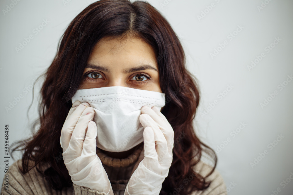 Portrait of a young woman holds hands on her head and has to stay home during quarantine due to coronavirus pandemia. Beautiful girl wearing medical mask and gloves. Covid-19 epidemia concept. Portrait of a young woman holds hands on her head and has to stay home during quarantine due to coronavirus pandemia. Beautiful girl wearing medical mask and gloves. Covid-19 epidemia concept.