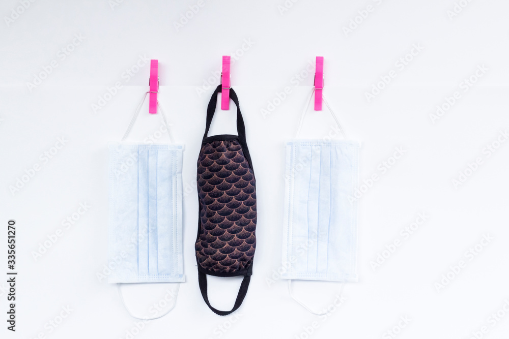 Handmade washable fabric face mask and surgical masks on white background hanging with laundry latch. Handmade washable fabric face mask and surgical masks on white background hanging with laundry latch.