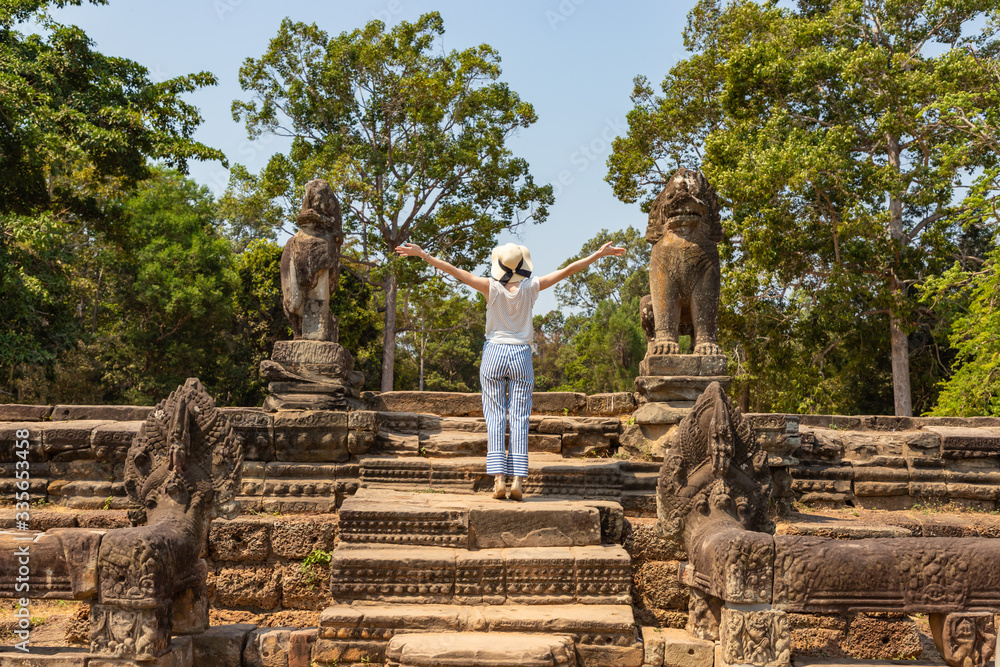 Young woman with raised hands stands on steps of ancient temple in Angkor Wat.. South Asia travel banner template. Cambodia.