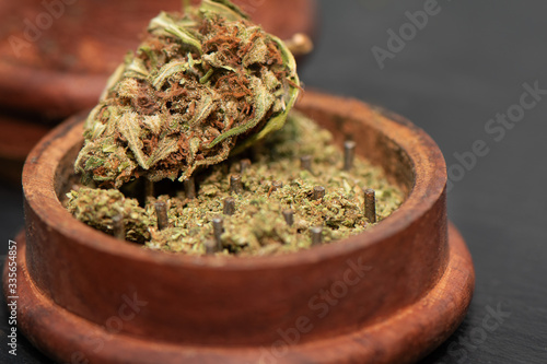 Close up of green dried marijuana bud lying at the top of wooden grinder