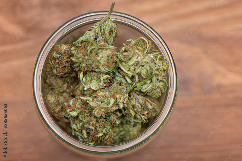 Top down shot of glass full of green dried cannabis buds on wooden table. Top down shot of glass full of green dried cannabis buds on wooden table.