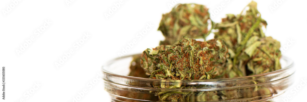 Shot of glass jar full of green dried cannabis buds on wooden table. 