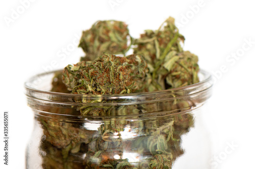 Shot of glass jar full of green dried cannabis buds on wooden table. 