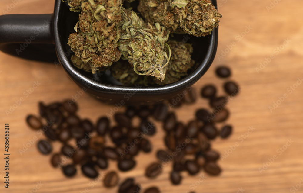 Top shot of black coffee cup full of dried green cannabis buds and some coffee beans on wooden table Top shot of black coffee cup full of dried green cannabis buds and some coffee beans on wooden table