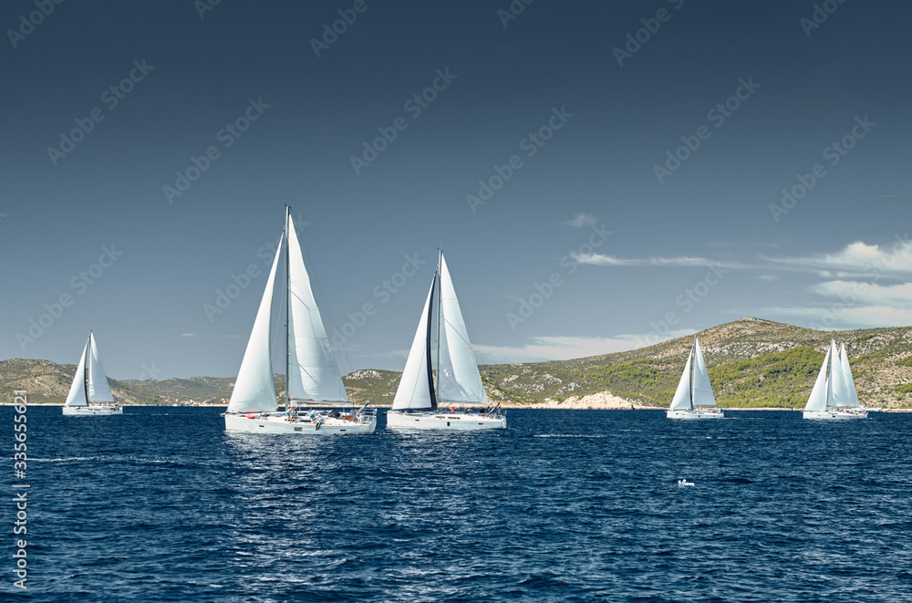 Fototapeta premium Sailboats compete in a sail regatta at sunset, race of sailboats, reflection of sails on water, multicolored spinnakers, number of boat is on aft boats, island is on background, clear weather