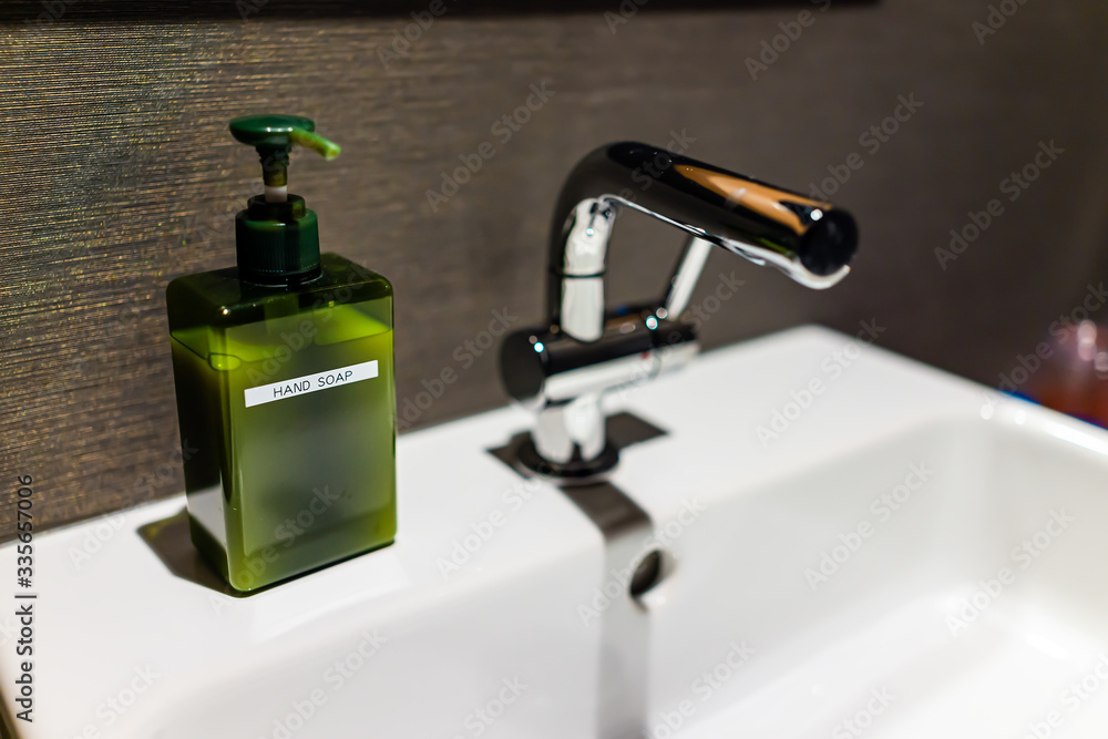 New modern faucet in bathroom closeup with stainless steel handle and white sink with green hand soap dispenser sign and dark background New modern faucet in bathroom closeup with stainless steel handle and white sink with green hand soap dispenser sign and dark background