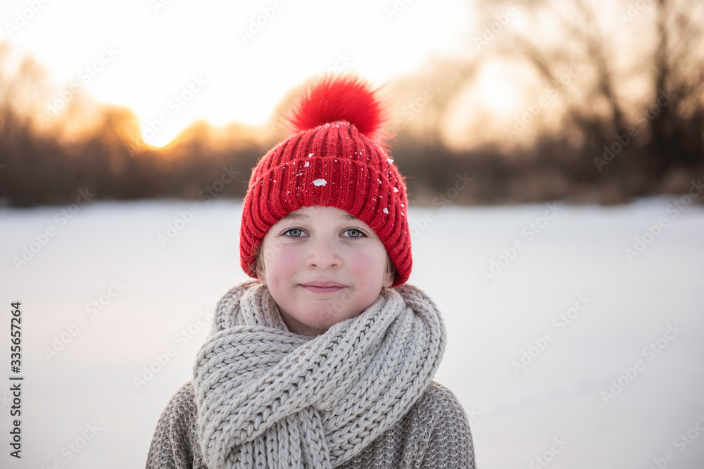 cute blond blue eye girl wearing bright red knitted hat with pom pom in a freezing cold snow coutdoor  nature walk