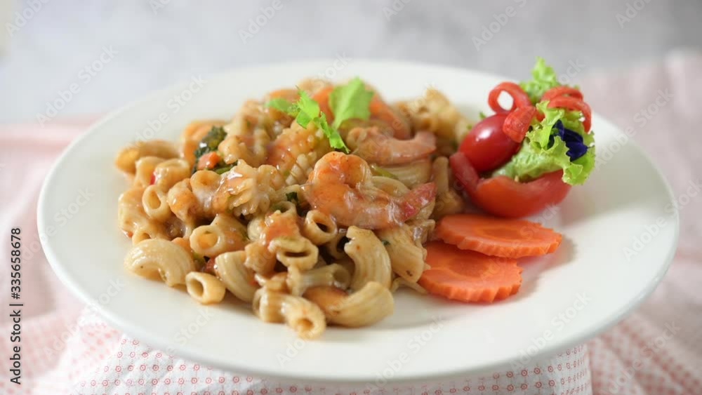 Stir fried macaroni with shrimp, squid, tomatoes, peppers and broccoli on a white plate Stir fried macaroni with shrimp, squid, tomatoes, peppers and broccoli on a white plate