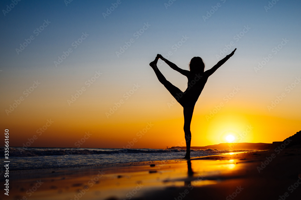 Girl at sunset, on the ocean shore doing yoga