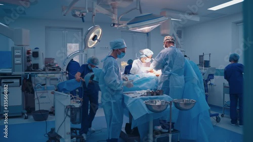 Team of surgeons doing plastic surgery in modern clinic. Group of medical workers in blue uniform perform an operation to a patient.