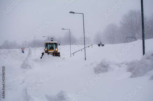 Yellow excavator clears the snow in the ski resort. Snowy days, road covered with snow. Winter landscape on mountain