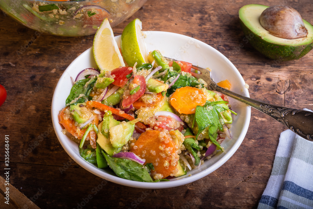 American vegetarian salad with vegetables, avacado, lettuce and quinoa in a plate with lime slices on a wooden table American vegetarian salad with vegetables, avacado, lettuce and quinoa in a plate with lime slices on a wooden table