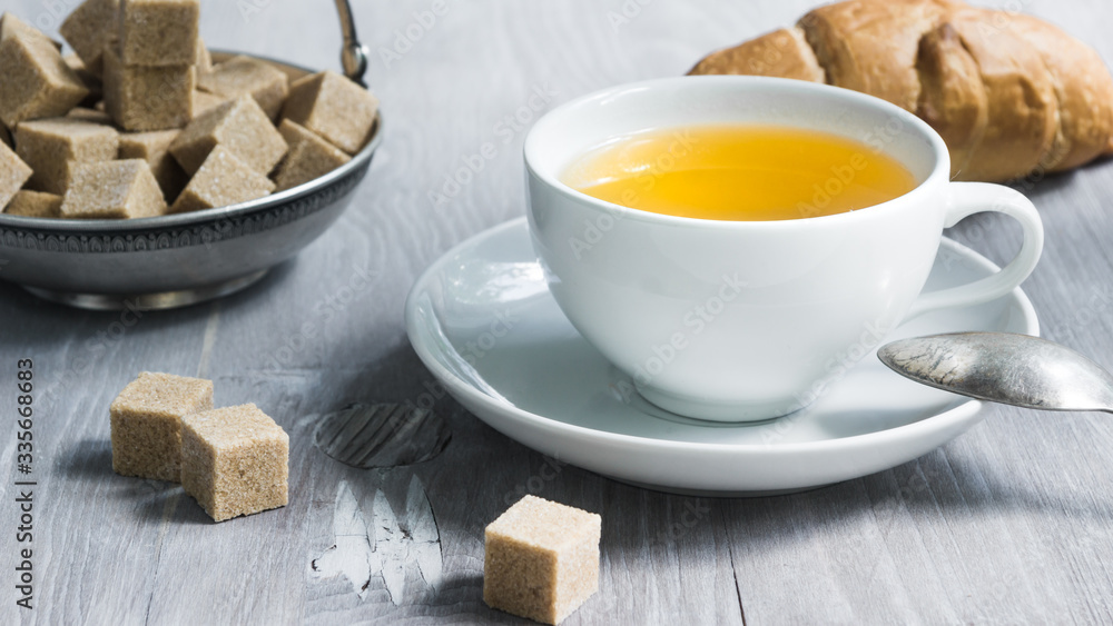 Cup of tea with croissant and pieces of sugar in a vase on a wooden table close-up Cup of tea with croissant and pieces of sugar in a vase on a wooden table close-up