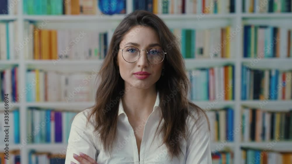 Portrait beautiful caucasian adult girl wearing glasses crossing arms looking vey confident at books library background. Pretty librarian. Portrait beautiful caucasian adult girl wearing glasses crossing arms looking vey confident at books library background. Pretty librarian.