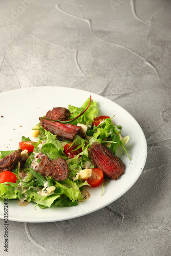 salad with beef steak cherry tomatoes and cheese in white plate on concrete table background
