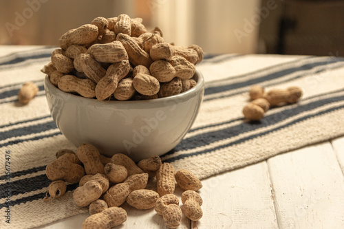 inshell peanuts in a white ceramic bowl on a cloth tablecloth and white wooden table