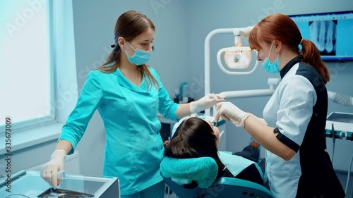 Patient at dentist's office. Female stomatologist together with assistant in medical uniform are treating woman's teeth in modern clinic.
