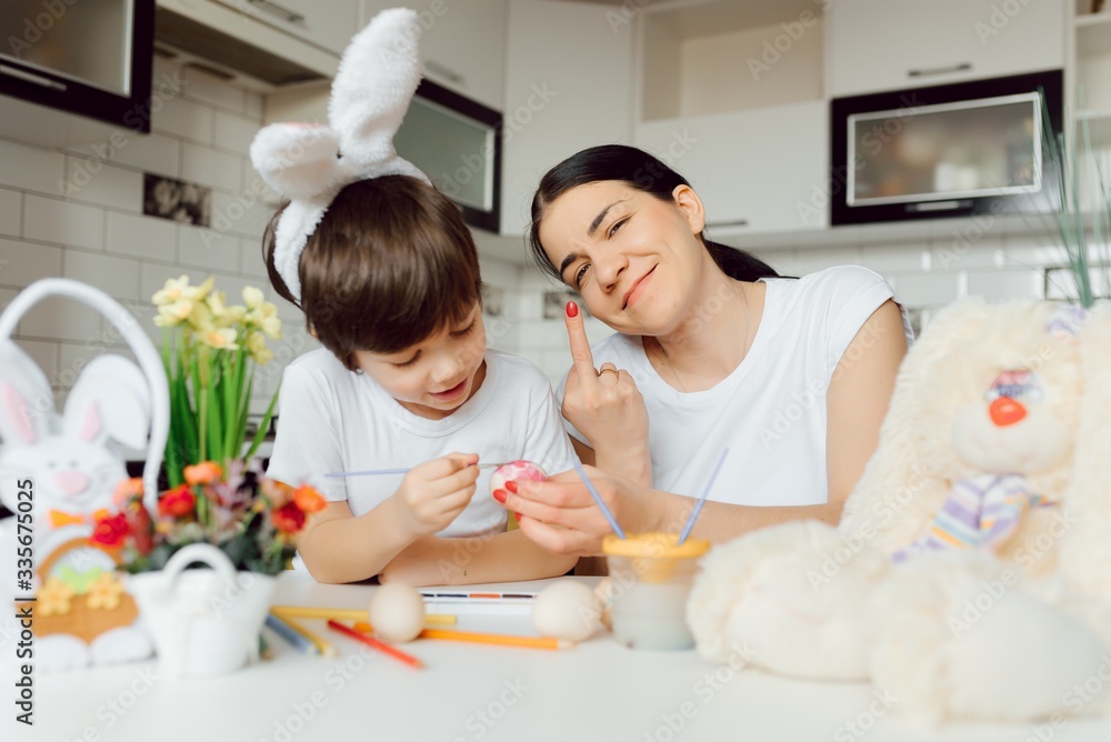 Mother and her son painting colorful easter eggs. Family celebrating Easter. Parent and kid play indoors. Decorated home and spring flowers. Mother and her son painting colorful easter eggs. Family celebrating Easter. Parent and kid play indoors. Decorated home and spring flowers.