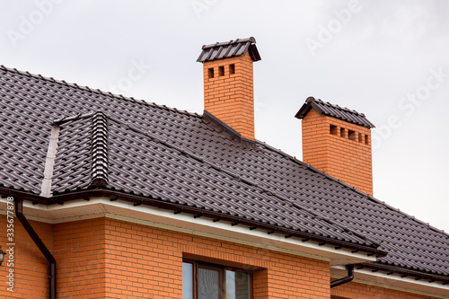 a brown rooftop of a ceramic tile with a pipe a storm drainage system, close up details of the architectural structure of brick house.