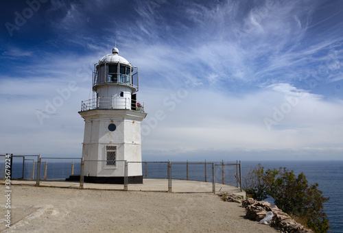 Old lighthouse on a high cliff, sea horizon and sky, sunny day. Travel and adventure, tourism.