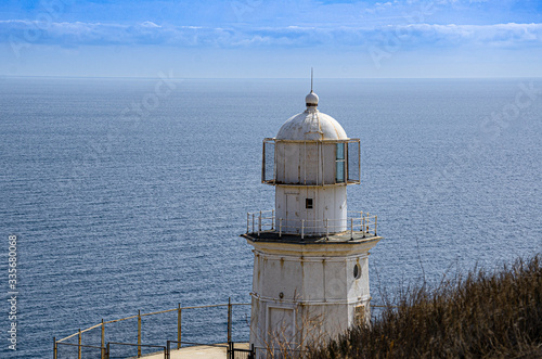 Old lighthouse on a high cliff, sea horizon and sky, sunny day. Travel and adventure, tourism.