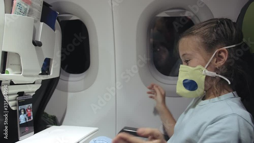 Little girl caucasian at plane with wearing protective medical mask. Child baby tourist at aircraft with respirator play at smartphone mobile phone. Coronavirus epidemic sars-cov-2 covid-19 2019-ncov. photo