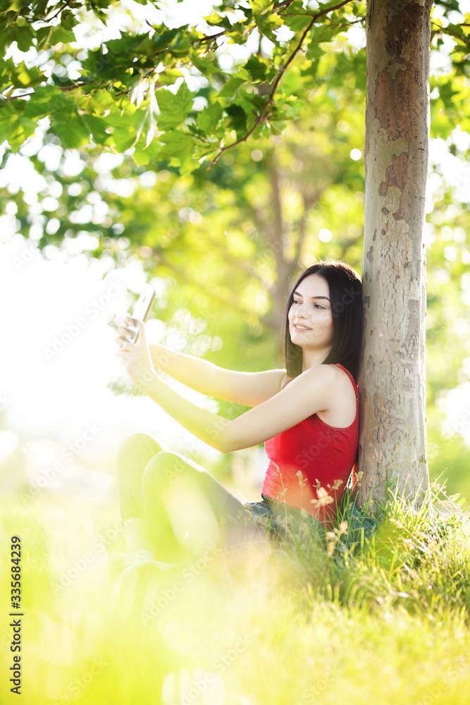 girl with dark brown hair using smartphone taking selfy under a tree girl with dark brown hair using smartphone taking selfy under a tree