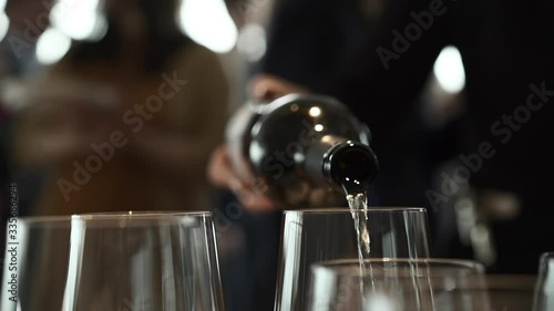A waiter in a restaurant pours white wine from a bottle by the glass. Holiday, party or romantic dinner.