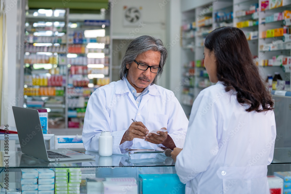 Two Professional Asian male and female pharmacist prepare prescription medicine capsule or supplementary food to patient in hospital pharmacy drugstore. Medical, pharmaceutical and healthcare concept.