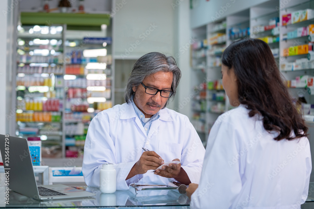 Professional Asian senior male pharmacist prepare prescription medicine capsule or supplementary food to female patient in hospital pharmacy drugstore. Medical, pharmaceutical and healthcare concept.