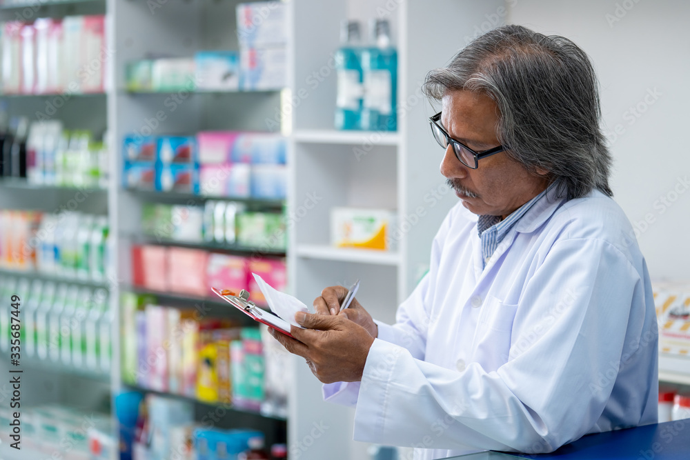 Professional senior Asian male Pharmacist checking medicines and health product inventory stock at hospital pharmacy or drugstore. Medical, pharmaceutics and personal healthcare concept.