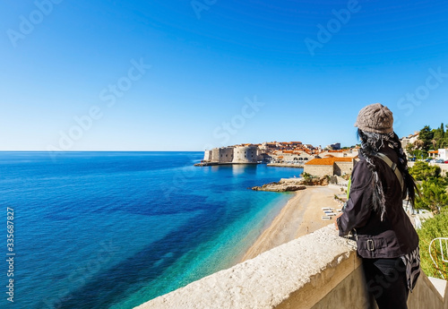 Back of woman enjoying beautiful landscape view of old town Dubrovnik, sand beach and blue Adriatic sea