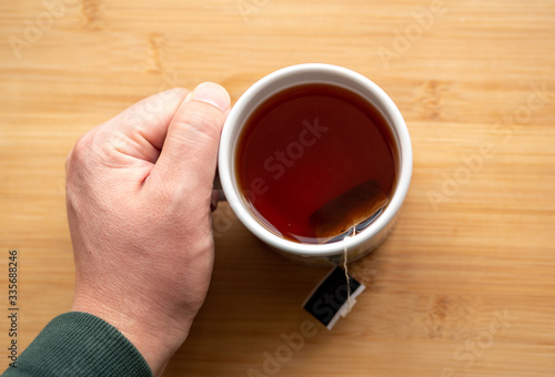 male hand holding cup of coffee on wooden background	