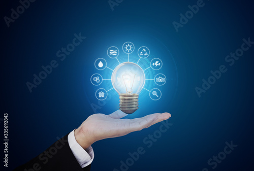 Hand holding bright light bulb with energy resources icon, on blue background. Energy concept