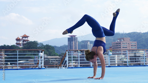 Beautiful flexible girl professional circus acrobat performer handstand, gymnastic bridge, backbend position, graceful woman on cruise liner, sports model on blue background, ship, Asian temple, city