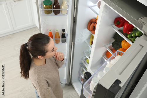 Young woman near open refrigerator indoors, above view