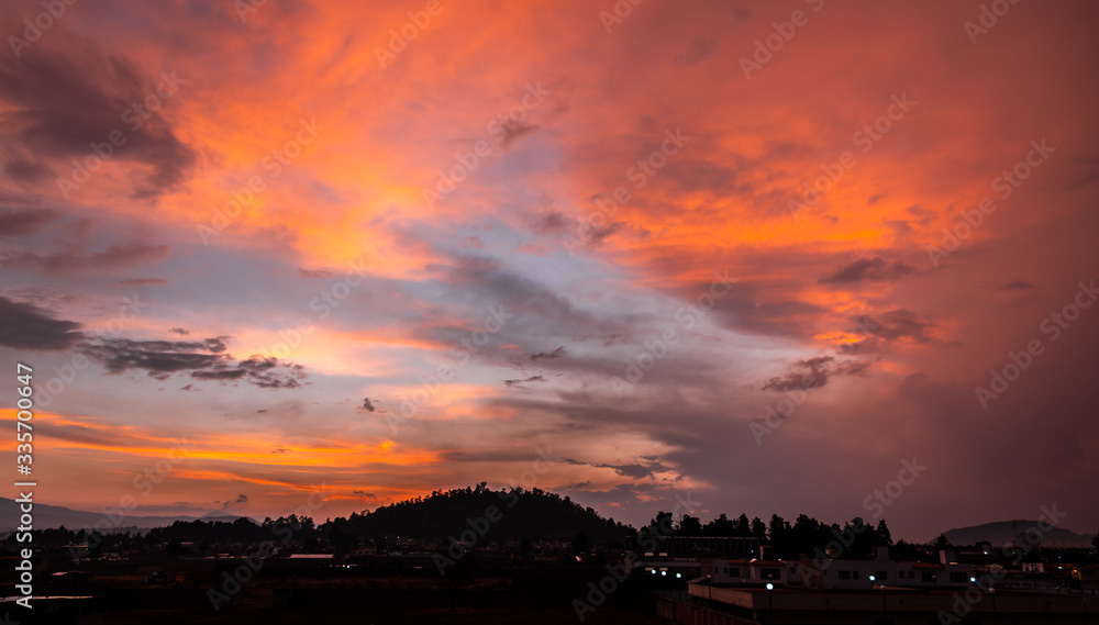 Sunset in a Mexican town called Metepec, with clouds painted in mertiolate color by the sun that hides on the horizon, distinguishes the characteristic Cerro del Calvario.