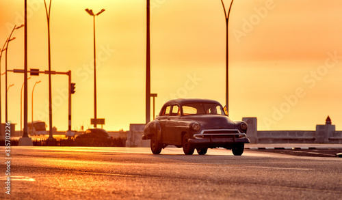 old classic american car driving though the streets of havana in cuba with the malecon in the background