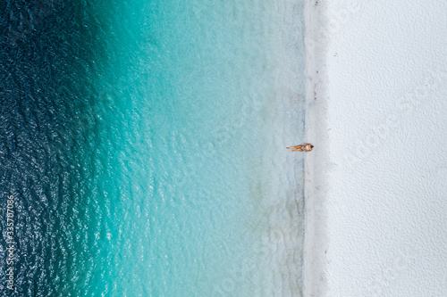 Obraz na plátne Beautiful girl lying on white sand on a stunning beach with blue crystal clear w