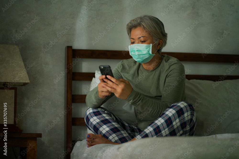 Fototapeta premium worried middle aged woman 50s with grey hair and protective mask checking online news with mobile phone during covid-19 virus home lockdown quarantine