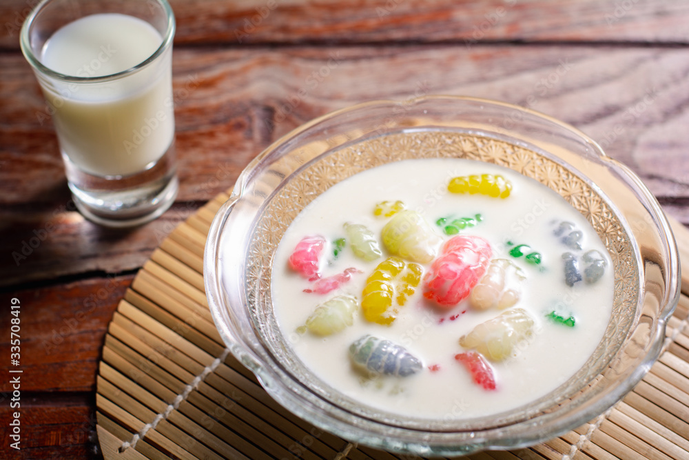 Colorful sweet rice gnocchi in fresh coconut milk in glass bowl on brown tablecloth on blackground. Delicious Thai desserts. Colorful sweet rice gnocchi in fresh coconut milk in glass bowl on brown tablecloth on blackground. Delicious Thai desserts.